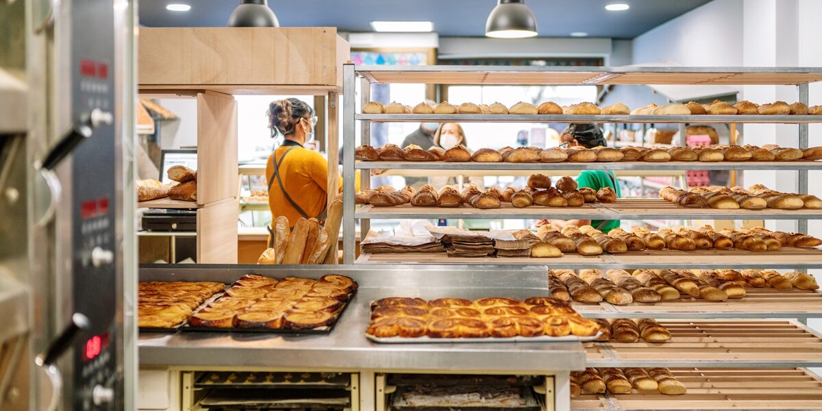 Rear view of a bakery with sales clerks selling bread to customers and carts with loaves and cakes fresh from the oven are seen and all are wearing face masks due to the covid19 coronavirus pandemic